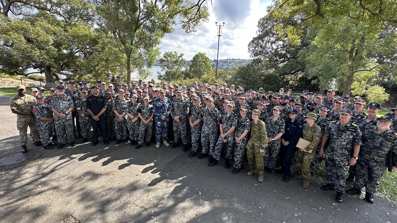 Image 1: Navy and Army Cadets and staff smiling for the camera in a group photo on Cockatoo Island.